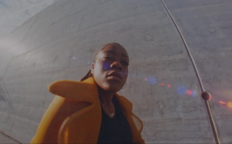 A young black woman poses in front of a concrete wall