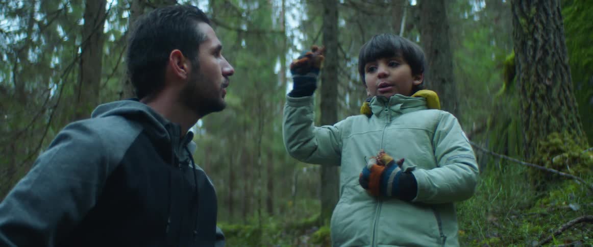 A boy chats with his father as they stand in the middle of a forest