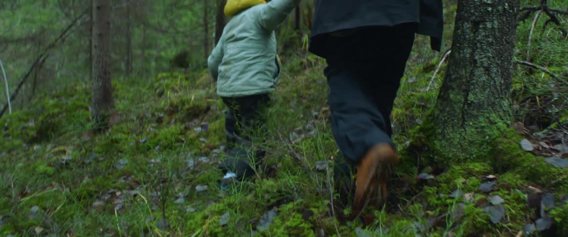 Father with navy blue coat and pants walks with son wearing light blue coat in the woods