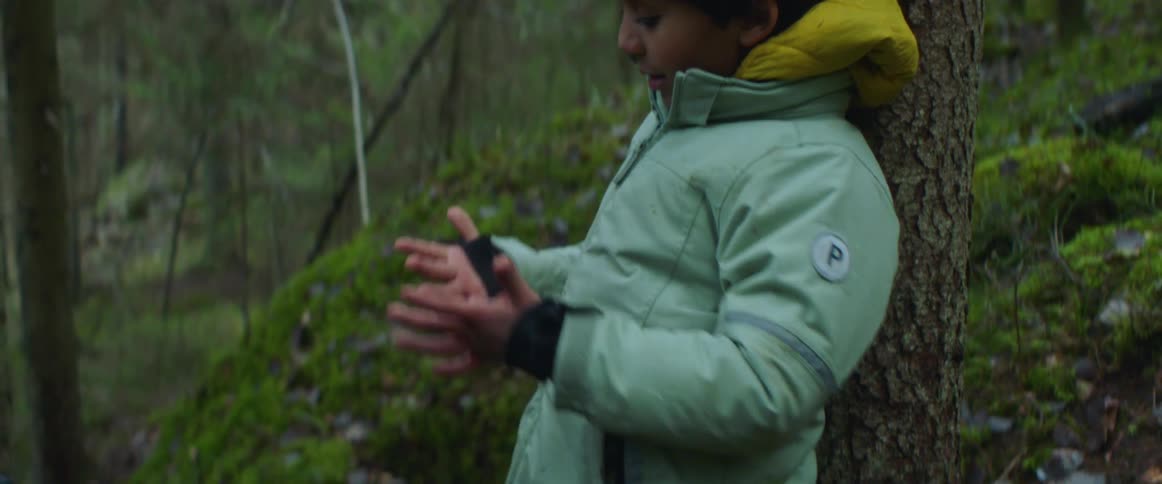 A woman is helping a boy put on his gloves while hiking in the forest in the daytime