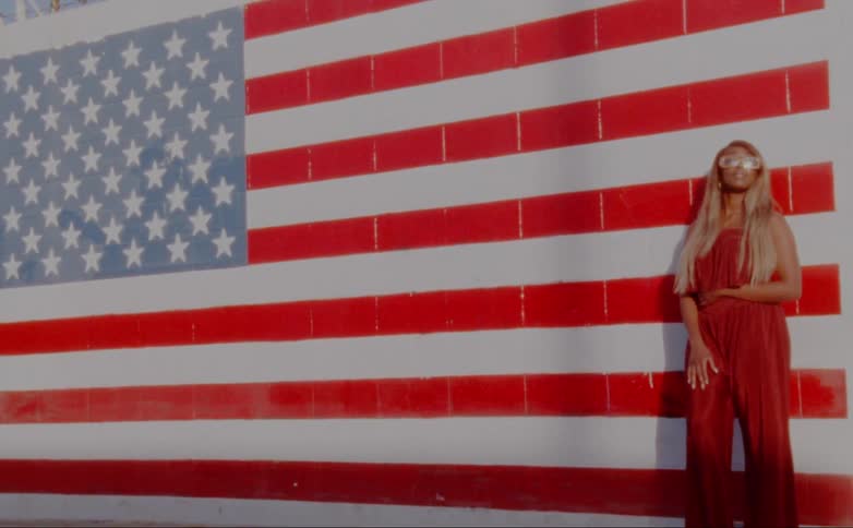 A woman stands in front of a wall painted with the american flag