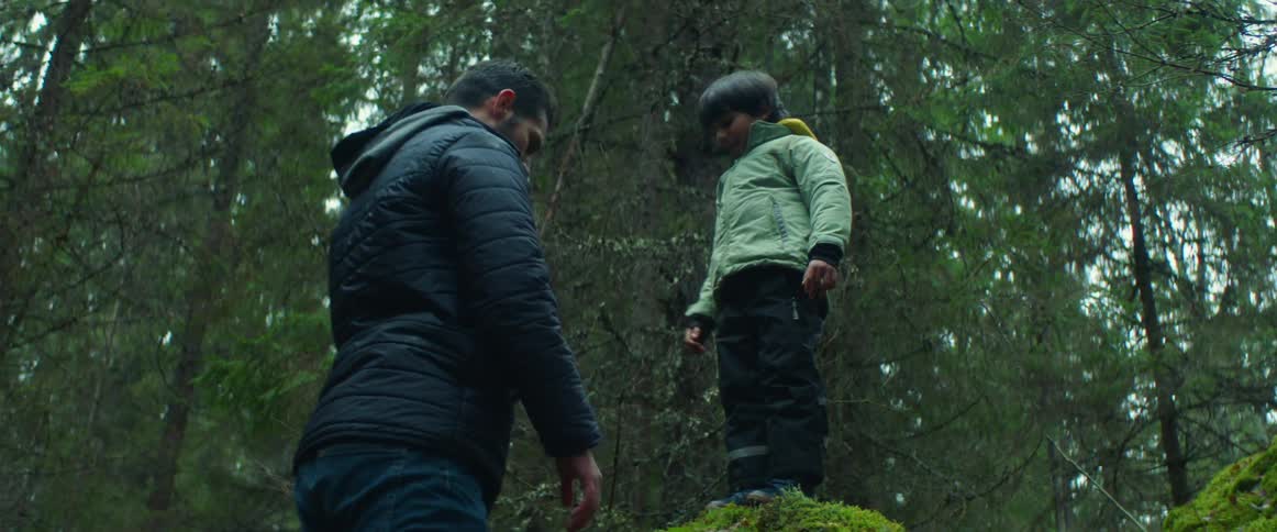 Man picks up boy and places him on moss covered boulder in forest