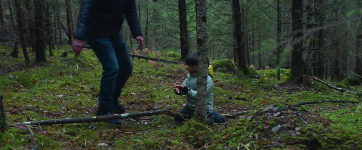 A man and boy play around in a heavily wooded area