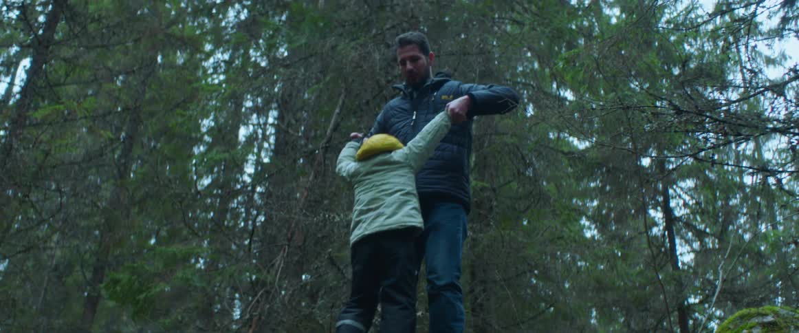 A man helps his son climb up moss covered boulders in a forest