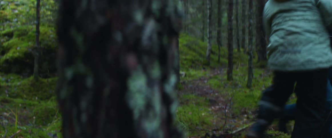 A man playfully runs as his son chases him in the forest