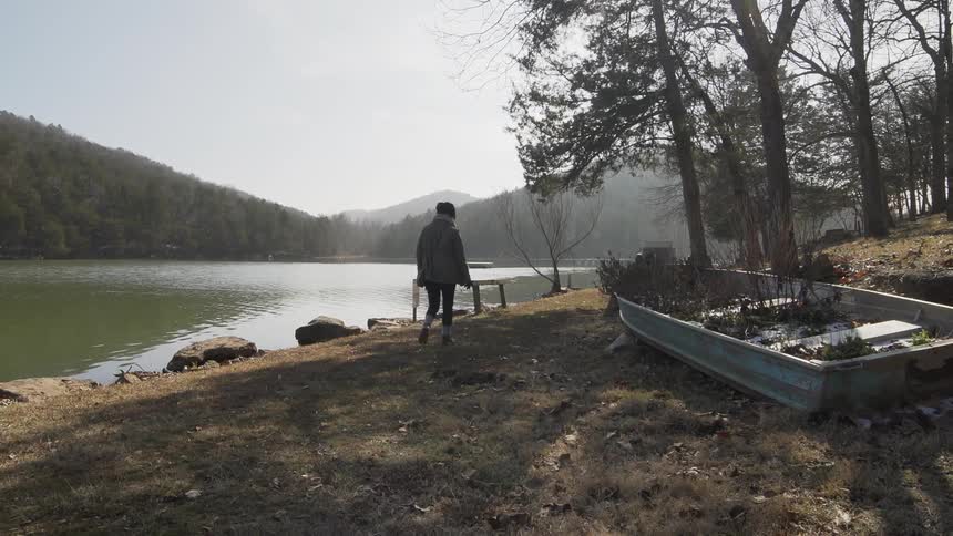 Woman walks near a lake while a boat rests in the grass