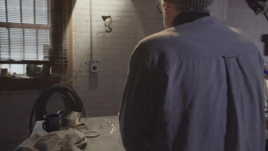 A man standing at a workbench holds a star up to the sunlight