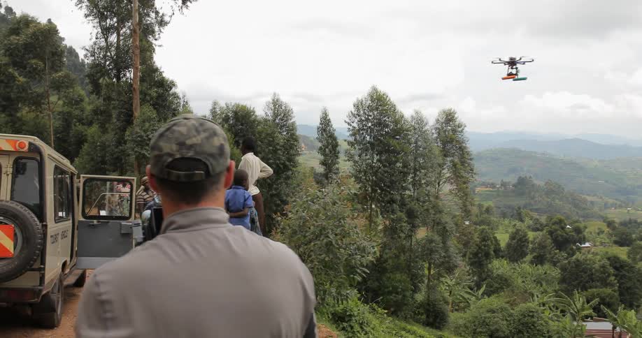 A photographer controls a drone with a camera near villagers on a dirt road