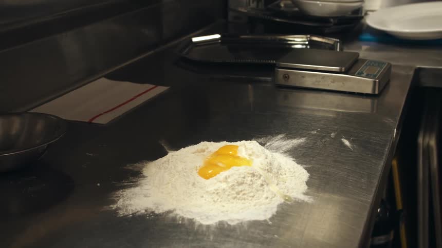 Close up of egg yolks dropping on a mound of flour
