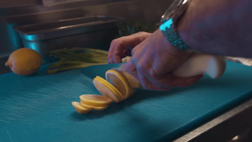 A person uses a knife to cut a piece of fruit into slices