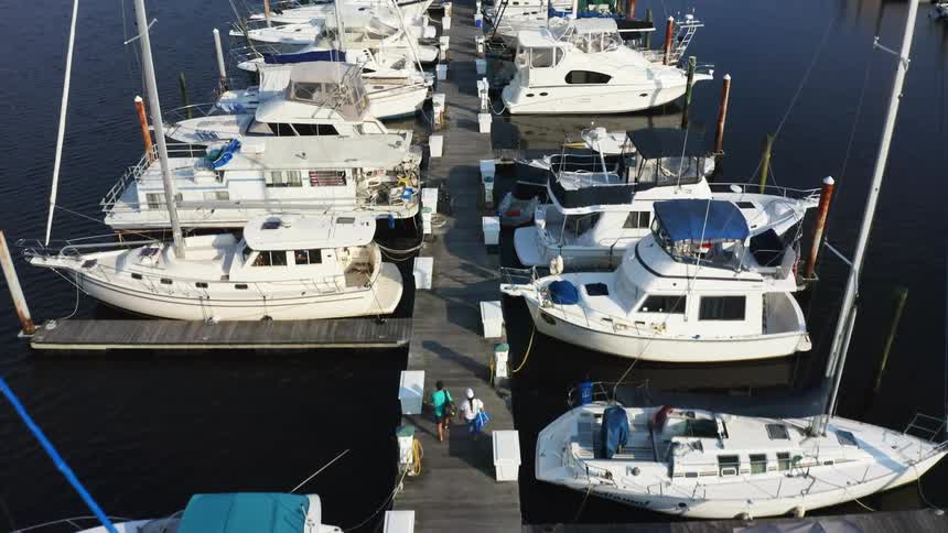 Two people walk on a dock in a marina with boats on both sides