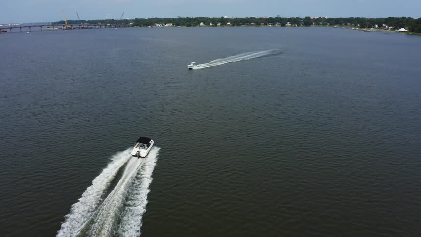An aerial view of two boat traveling quickly on a large lake during the daytime with a waterfront community in the background
