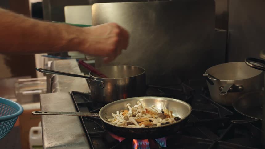 A professional cook adds food to a pan in a commercial kitchen