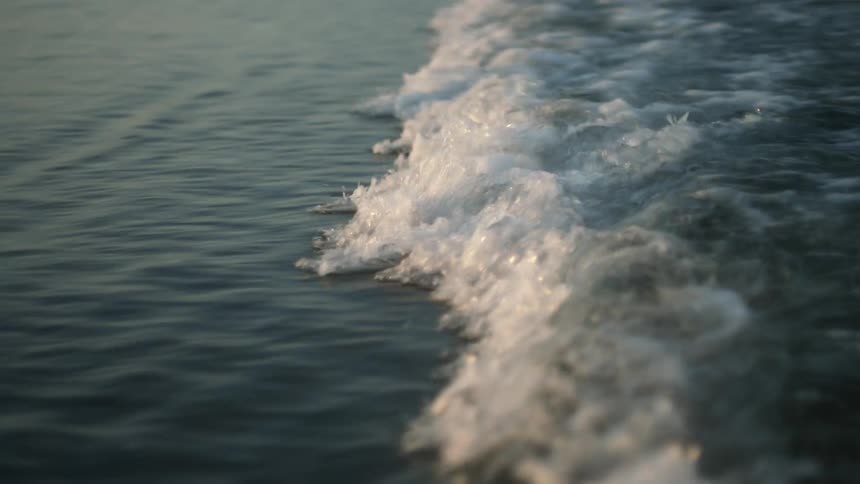 Waves splash as they roll onto shore near the feet of people walking on the beach
