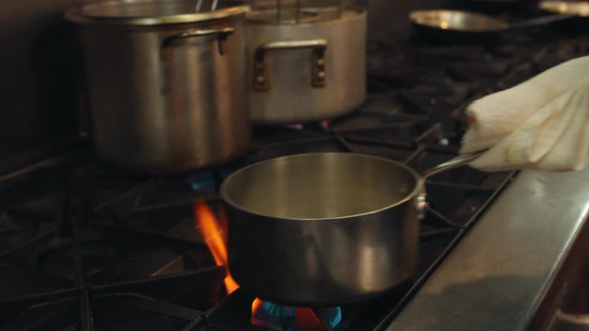 A person is cooking rice in a pot over a restaurant stove top