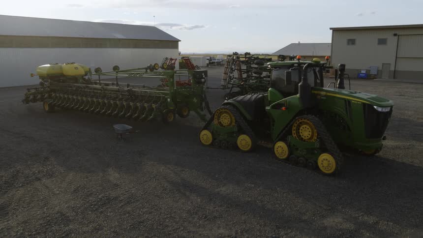 Low pullback reveal over a large green tractor parked in a farm yard along with other equipment