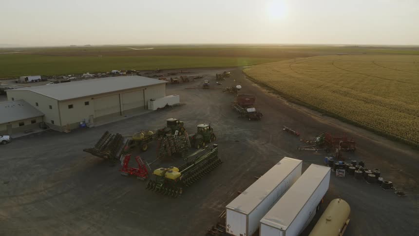 Trucks and farm machinery sit between sheds on a hot and sunny morning