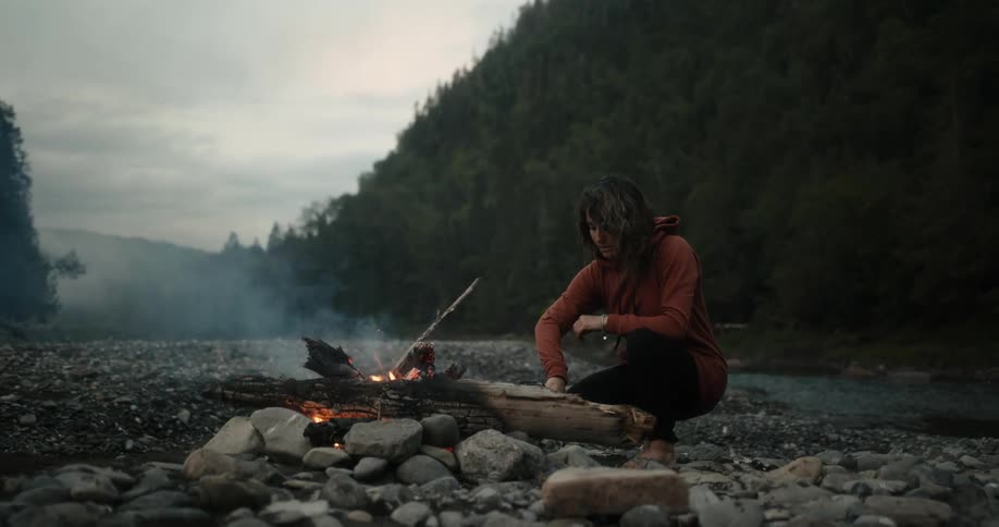 A woman is stirring the flame in the campfire