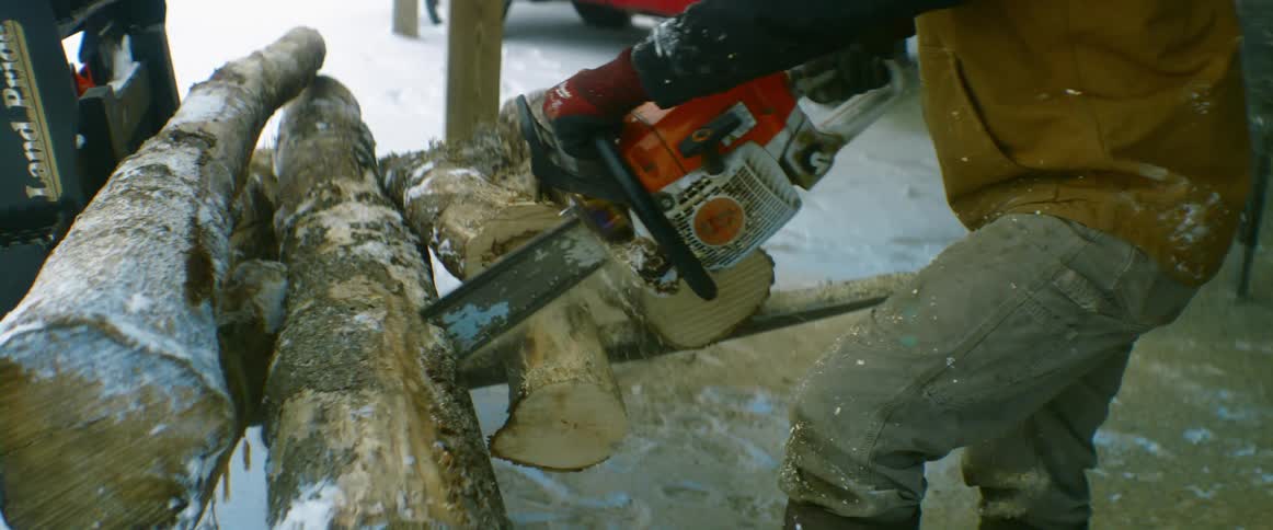 A man uses a chainsaw to cut wood