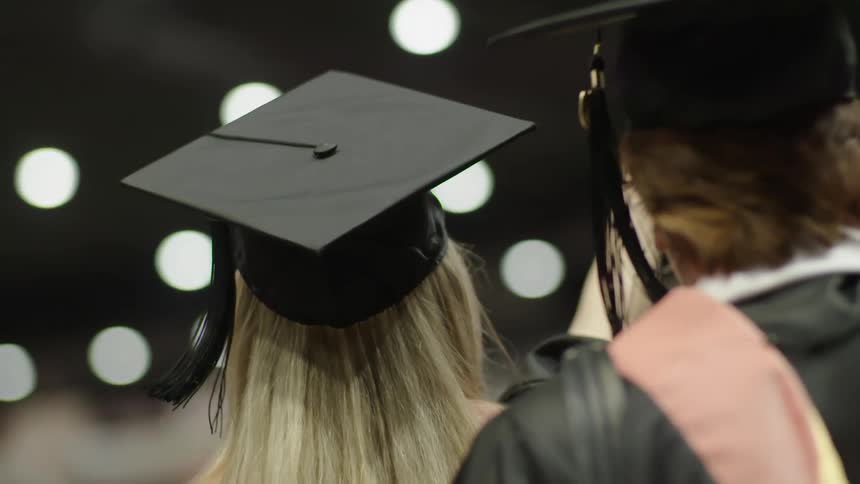 Man and woman in graduation outfits wave with their right hands