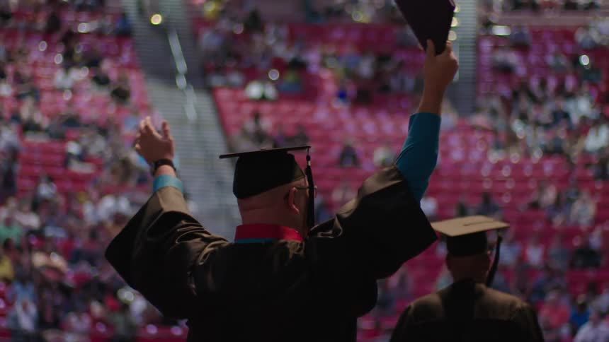 A man waves his arms in the air as he walks the stage during graduation