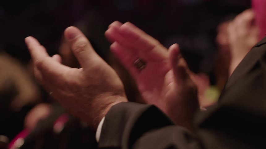 White man wearing a ring a white shirt and a black suit sitting in the audience and clapping