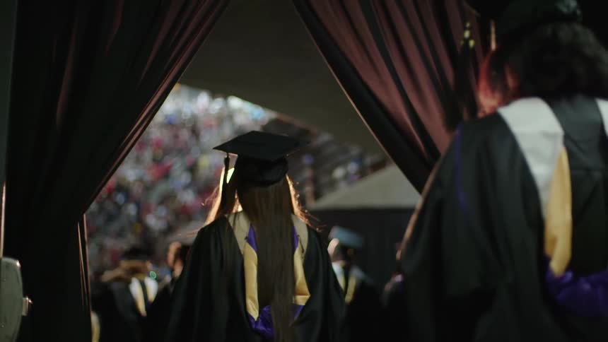 Students walk through curtains heading to an outdoor stadium for granduation