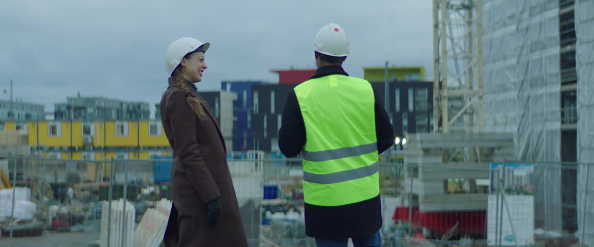 Construction worker holds a clipboard and talks and laughs with a woman at a construction site