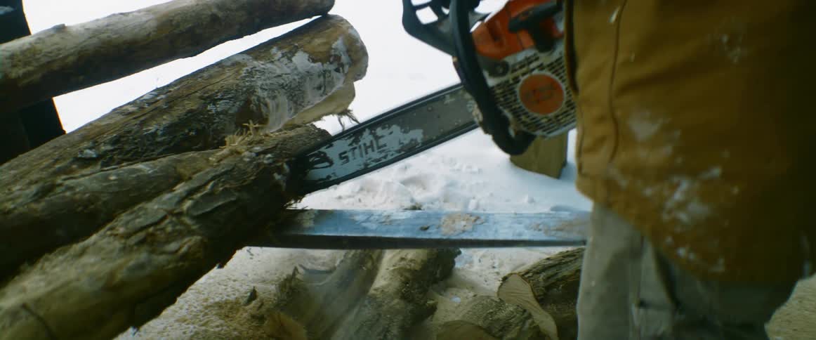 A man cutting wood outdoors in the snow with a chain saw
