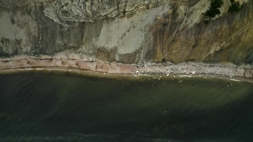 People swim on the ocean and play on the beach below a cliff