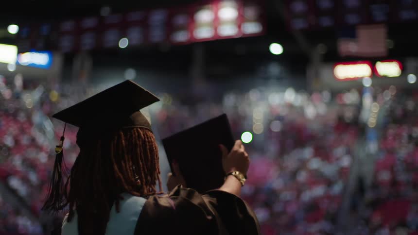 Woman at a graduation ceremony holds up her diploma to the crowd