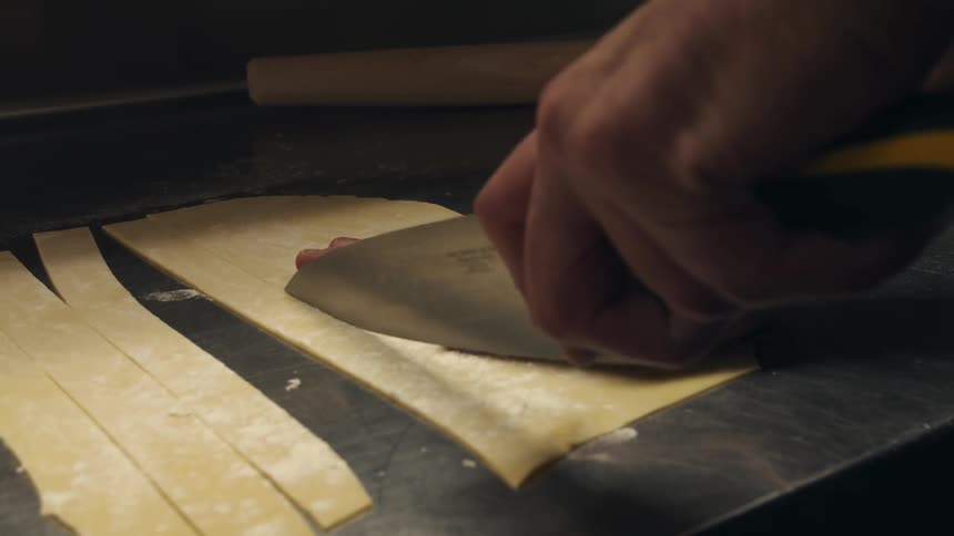 A person uses a large knife to cut fresh made pasta dough
