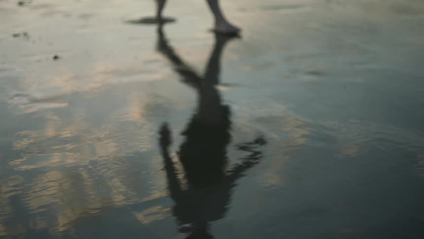 Man walking at the wet sand on the beach with his body reflecting on the ground