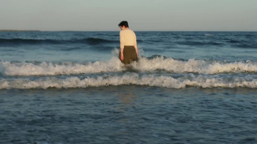 White woman walking alone in the water at the beach with tides reaching the coast