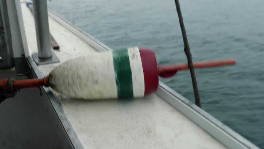 A man reaches over the side of a boat and pulls a buoy out of the water