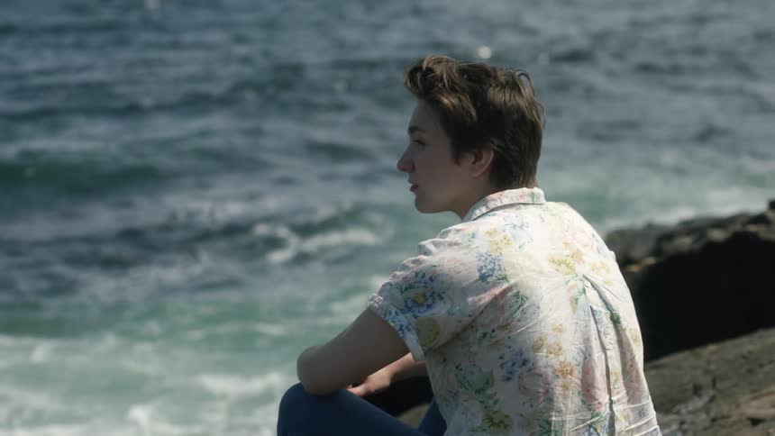 A woman sits on the rocks of the beach