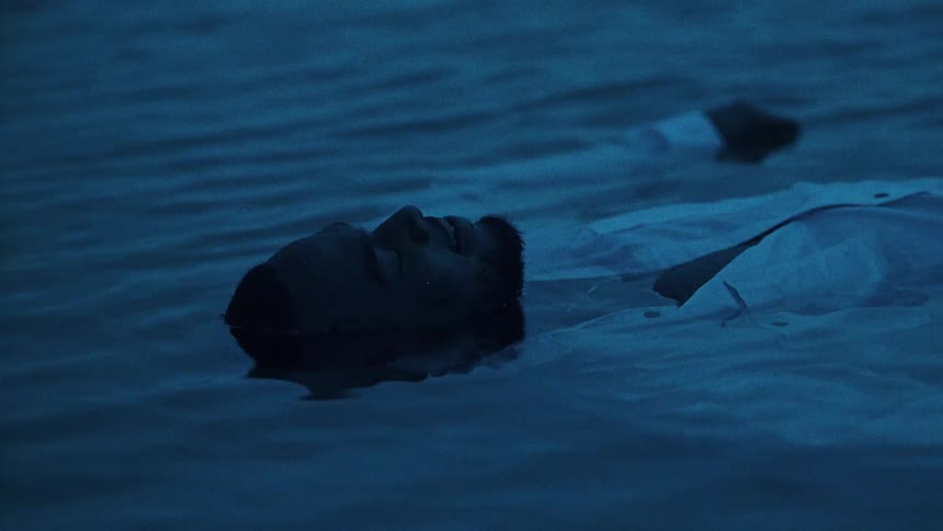 Black man wearing a white shirt lying on his back in the water