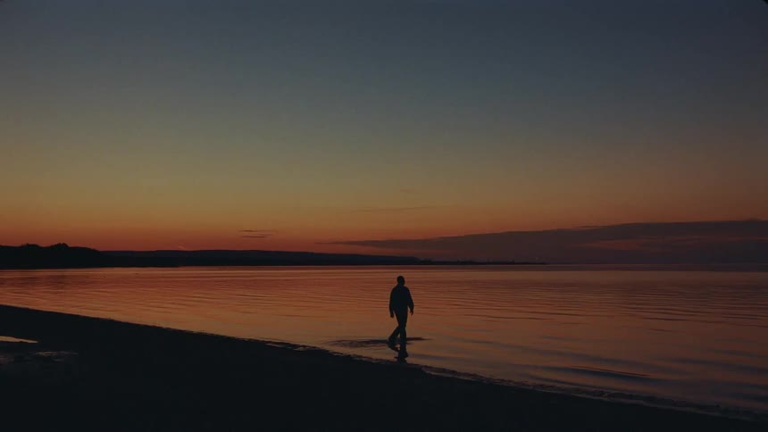 Silhouette of a man on a beach walking into the water as the colors of the red sky reflect onto the water