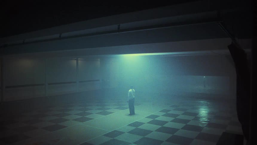A man in a large recreation room stands up and slowly walks away toward a large mirror