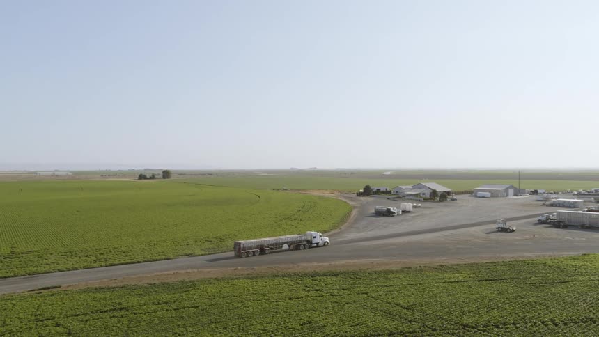 A large truck transporting fresh produce rolls into a farmyard between circular crop fields