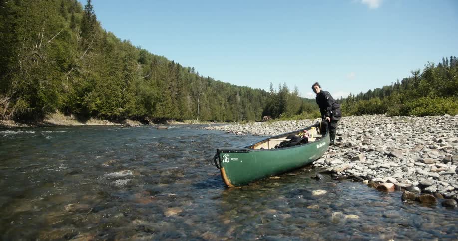A person stands beside a river getting a canoe ready in the water