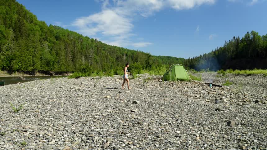 A young woman walks away from a river and towards her tent