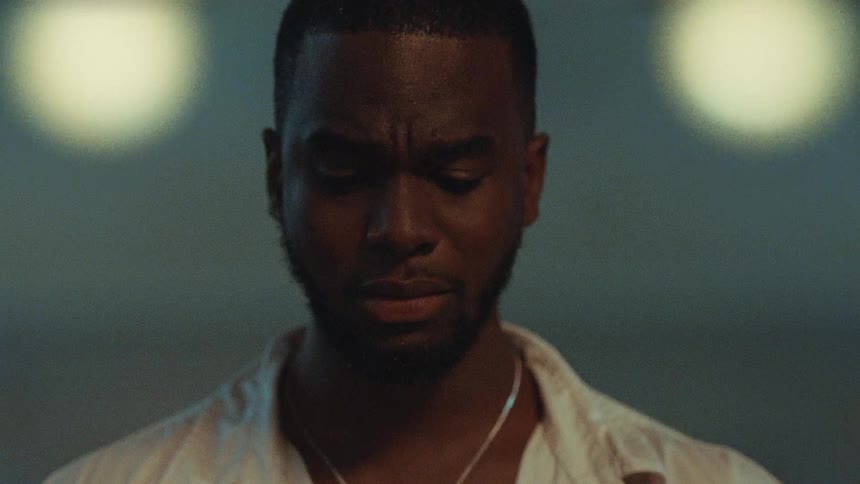 Black man wearing a chain around his neck looks down as he thinks