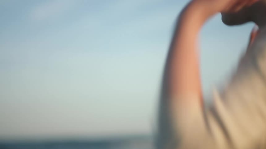 A woman on the shore reaches down and wets her hands in the water and rubs her hair