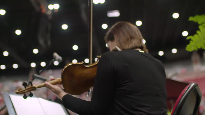 A woman plays the violin during a concert at a crowded stadium