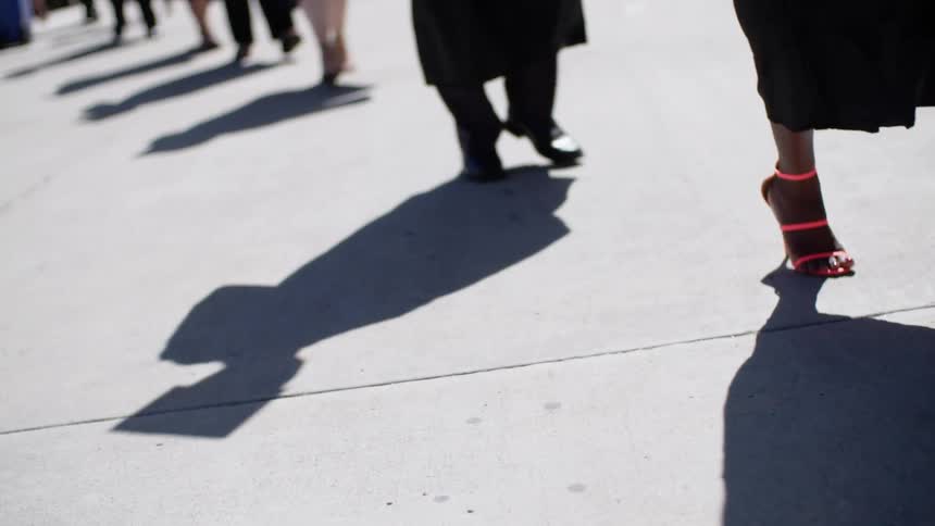 A group of men and women walk along the concrete sidewalk