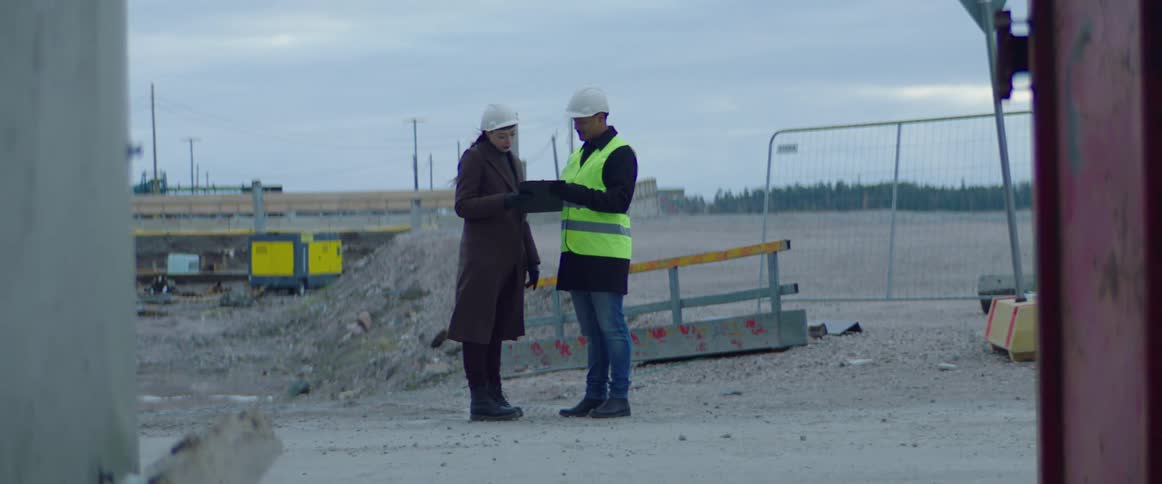 Construction worker holds a clipboard and talks with a woman on the construction site