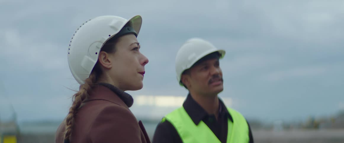 Construction worker holding a clipboard talks with a woman at a construction site