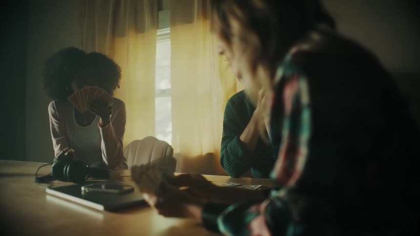 Three female friends sit at table smiling while playing a card game