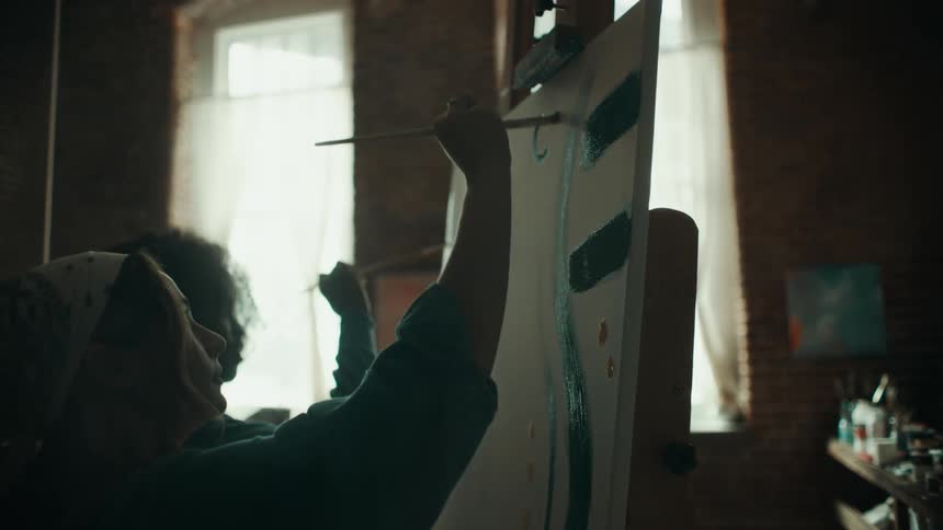 Two young girls painting a blank canvas together in a room inside the house